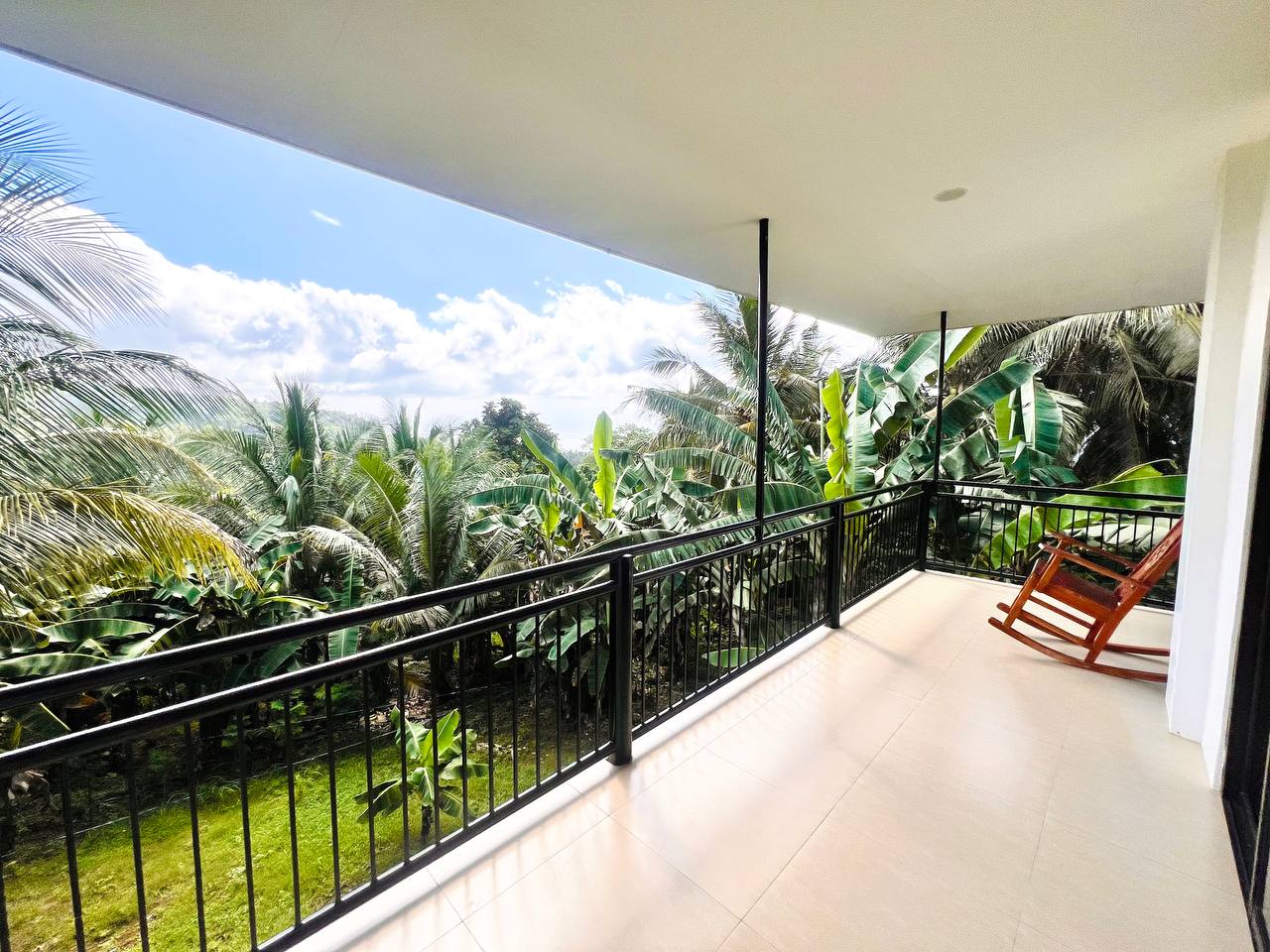 A rocking chair on a balcony looking over banana leaves and palm tops