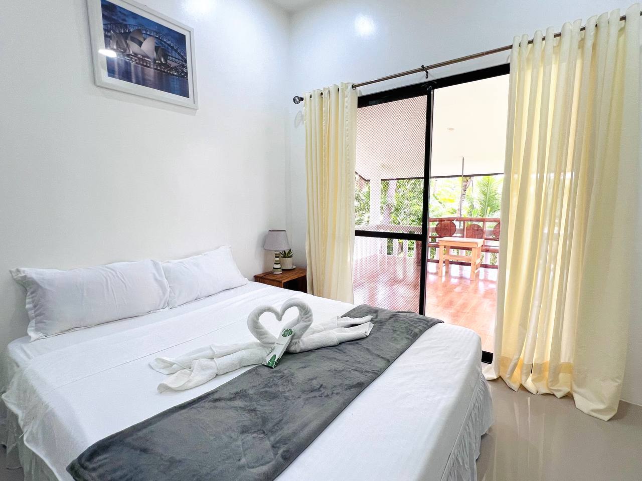 A made bed with towels folded into a heart, beside sliding doors leading out to a timber balcony