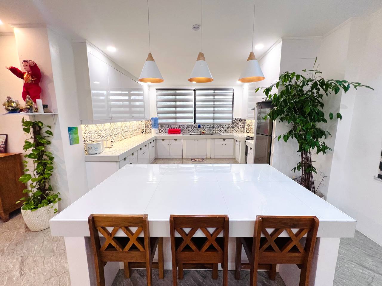 A white kitchen with three pendant lights over a wide island and patterned tile behind the counter