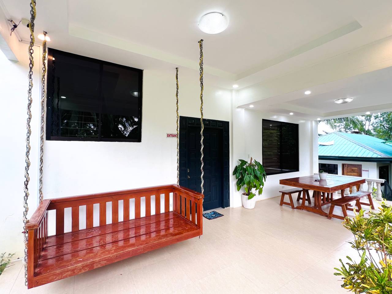 A hanging timber bench on a covered porch beside a dining table