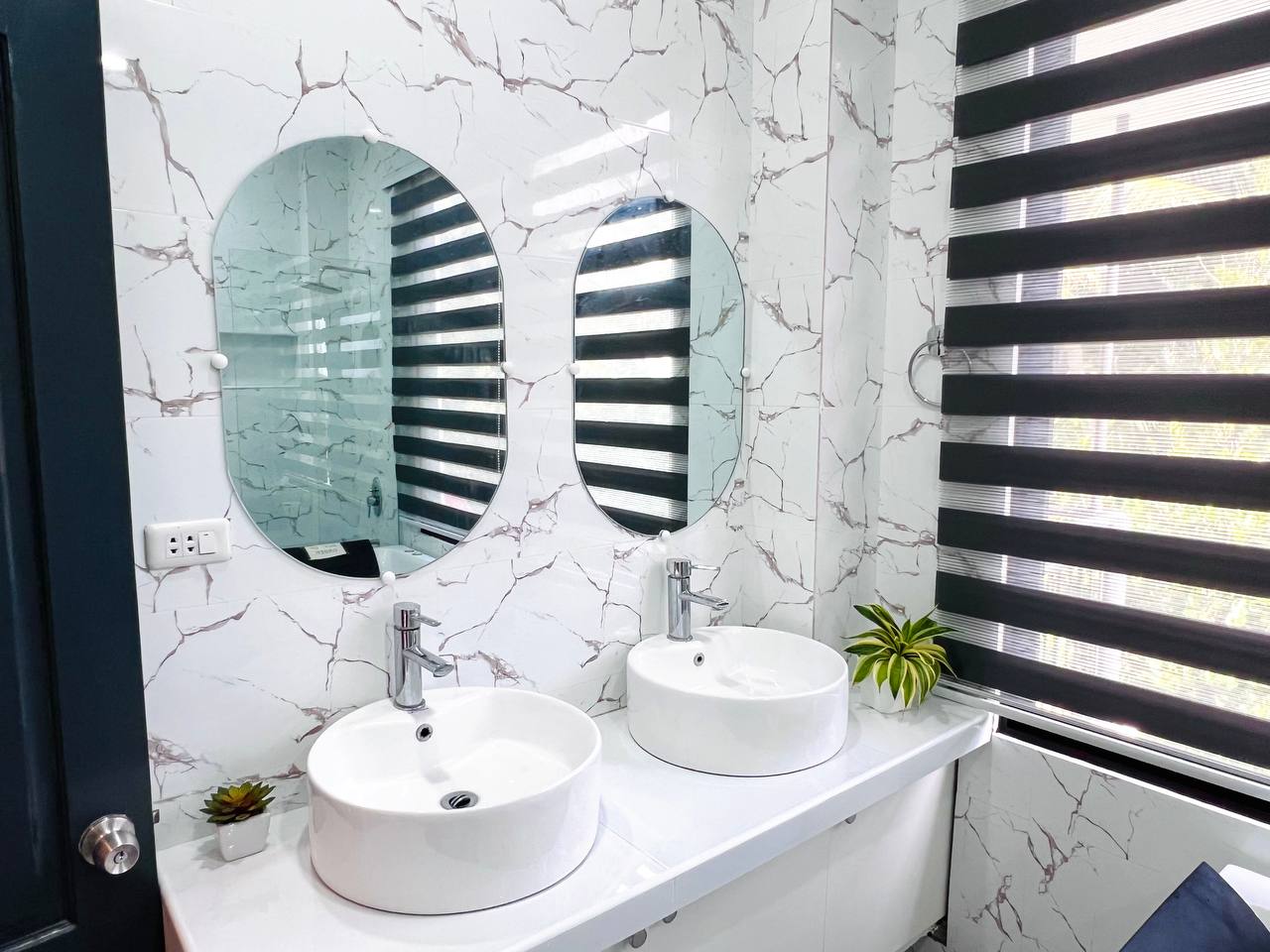 Twin round basins under two oval mirrors against marble tile