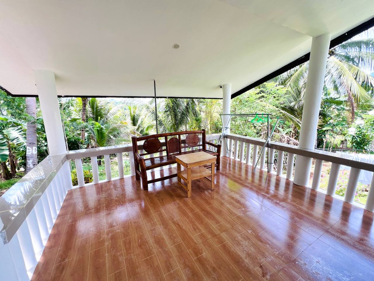 A covered veranda with polished timber floors, a carved bench and a low table looking into the trees