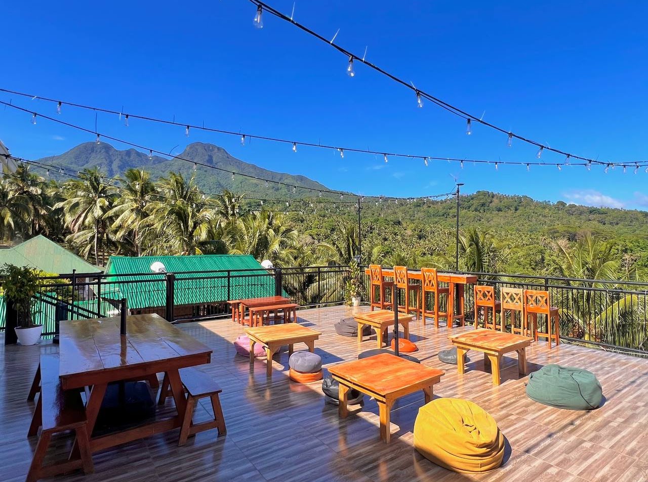 The rooftop deck at dusk with festoon lights strung above low tables and the Camiguin volcanoes behind
