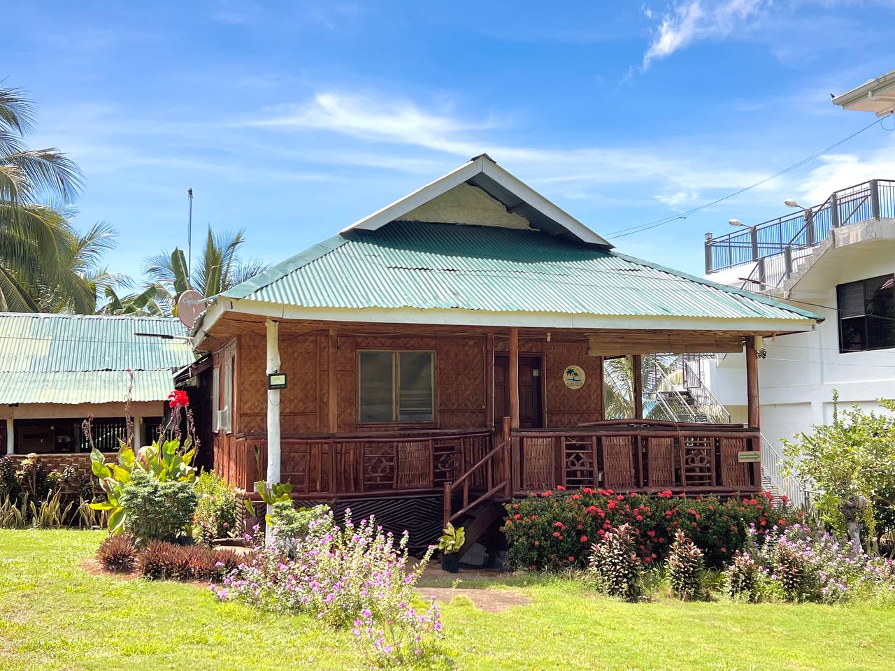 The Bamboo Villa, a woven cottage with a green roof and flowers along the steps